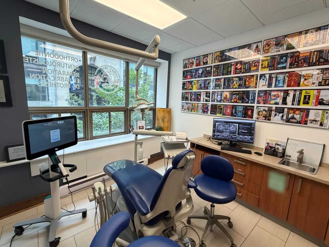 A treatment room: a blue dental chair by the window, and a wall covered with film covers